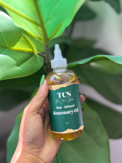 Bottle of The Chic Studio Sun Infused Rosemary Oil 8oz held in front of green leaves
