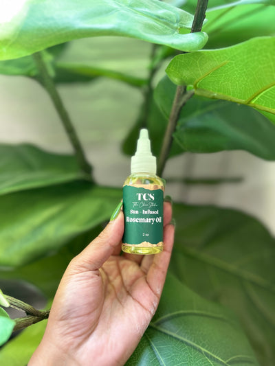 Hand holding a bottle of TCS Rosemary Oil 2oz against a green leafy background