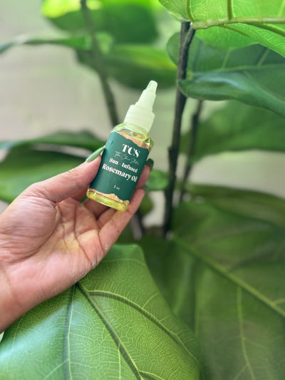 Hand holding a bottle of TCS Rosemary oil against a green leafy background