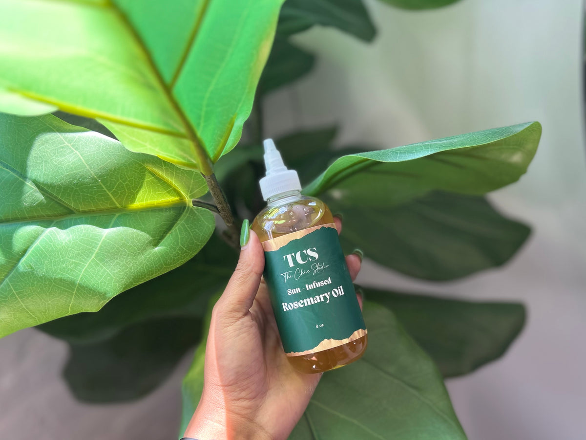 Hand holding a bottle of The Chic Studio Rosemary Oil 8oz against a green leafy background