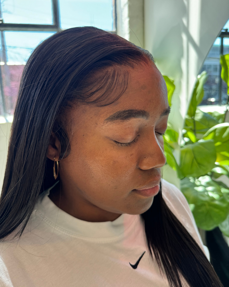 Person wearing a white Nike shirt and a frontal medical wig with plants in the background
